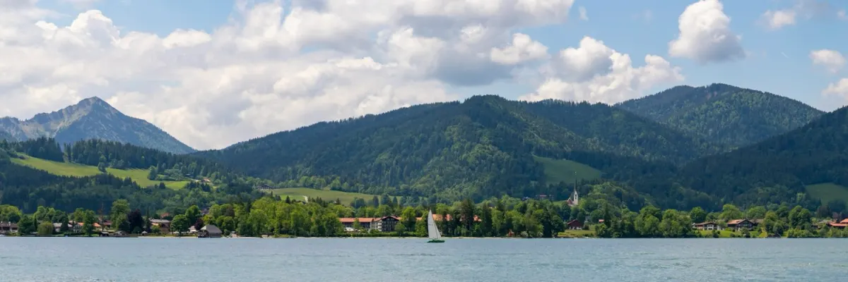 Tegernsee mit Segelboot vor grünen Bergen an einem Sommertag